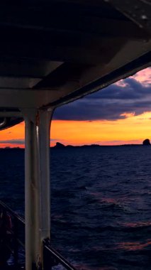 Vertical video. Ferry View Through Metal Frame Toward Bright Orange Sunset Over Calm Sea with Distant Islands Evening Serenity
