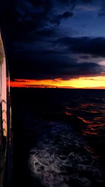 Vertical video. Sunset View from Ferry Deck with Dark Waves and Glowing Orange Horizon as Ship Moves Through Calm Evening Sea