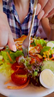 Vertical video. Close-Up View of a Person in Checkered Shirt Cutting Grilled Chicken Over Fresh Salad with Vegetables and Boiled Eggs, Healthy Eating Concept