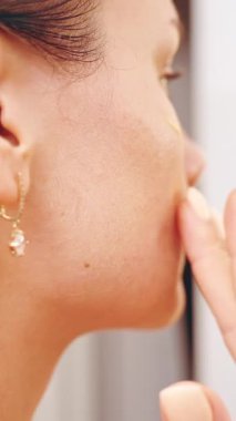 Dikey video. Kadın Nazikçe Retinol Serumunu Parmak uçlarıyla Yanağa Sürterken Aynaya Bakarken, Cilt ve Parıltı, Güzellik ve Sağlık Konseptine Odaklanıyor