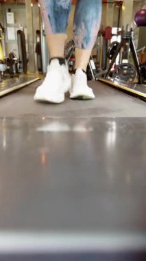 Vertical video. Dynamic Close Shot of Woman Sneakers on Treadmill Capturing Forward Step with Motion Blur in Bright Gym Light, Cardio and Determination Concept