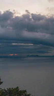 Vertical video. Dramatic Cloudy Sky over Calm Sea with Small Islands on Horizon during Golden Sunset Viewed from High Point, Sunset Timelapse Concept