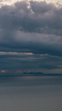 Vertical video. Bright Sun and Thick Clouds over Tranquil Ocean with Islands in Distance Illuminated by Warm Light, Sunset Timelapse Concept