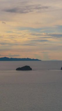 Vertical video. Small Islands in Calm Ocean Under Colorful Sky with Deep Blue Clouds and Orange Light, Sunset Timelapse Concept