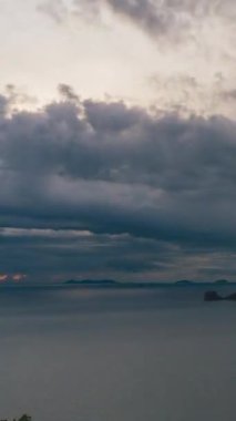 Vertical video. Ocean View with Islands Silhouetted Against Yellow and Orange Sky under Dark Clouds at Twilight, Sunset Timelapse Concept