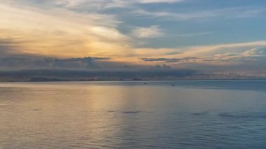 Calm Sea with Soft Sunset Light and Distant Islands Beneath Layered Clouds Creating Warm Golden Reflection, Sunset Timelapse Concept