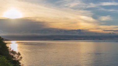 Golden Sun Reflected on Calm Ocean Near Green Cliff with Distant Islands on Horizon Under Clear Sky, Sunset Timelapse Concept