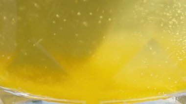 Slow Motion Macro View of Spoon Stirring Yellow Liquid in Transparent Glass with Soft Light and Gentle Bubbles, Close-Up Angle, Refreshing Drink Concept