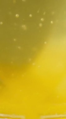 Vertical video. Slow Motion Macro View of Spoon Stirring Yellow Liquid in Transparent Glass with Soft Light and Gentle Bubbles, Close-Up Angle, Refreshing Drink Concept