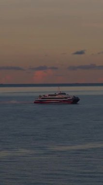 Vertical video. Passenger Ferry Travels Across Calm Sea Toward Distant Horizon During Sunset with Soft Clouds and Dimming Light in Wide Angle Scene
