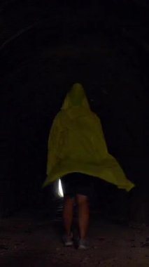 Dikey video. Sarı Yağmurluklu Kadın Umut ve Kefaret Konseptini sembolize eden Karanlık Tünelin Sonundaki Parlak Işığa Doğru Yürüyor