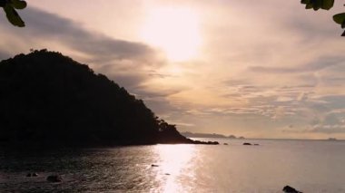 Sun Setting Behind Island Silhouette Reflecting on Calm Sea Surface, Captured from Wide Angle for Time Lapse Effect, Sunset Transition Concept