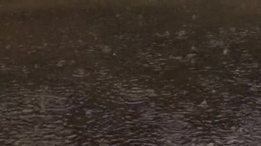 Rain Hitting Brown Water Surface Forming Splash Patterns and Ripples, Close Up Rainfall Scene Concept