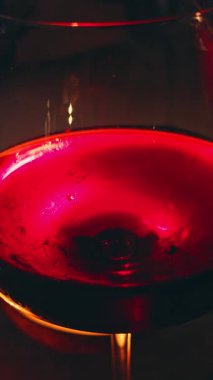 Vertical video. Red Wine Being Poured into a Glass Near Candlelight Creating Warm Reflection and Swirling Motion, Romantic Evening Concept