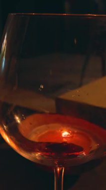 Vertical video. Red Wine Pouring into Glass with Candlelight Reflections and Another Glass Nearby on Table, Romantic Dinner Atmosphere Concept
