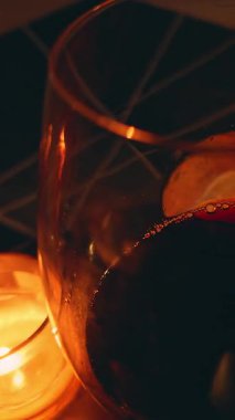 Vertical video. Close Up of Red Wine Being Poured into Glass Near Burning Candle and Box on Wooden Table, Relaxed Evening Concept