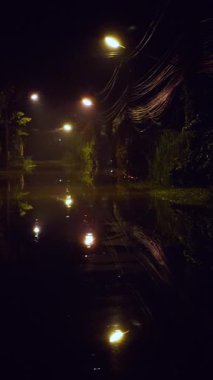 Dikey video. Gece Yağmurdan Sonra Mavi ve Sarı Işık Yansımaları ile Sel Altındaki Sokak, Durgun Su ve Sessizlik Konsepti
