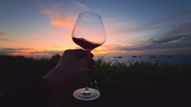 El ele tutuşan kırmızı şarap kadehi canlı günbatımına karşı Okyanus ve Gece Parıltısı Adaları, Rahat Yaşam Tarzı Kavramı ve Huzurlu Anlık