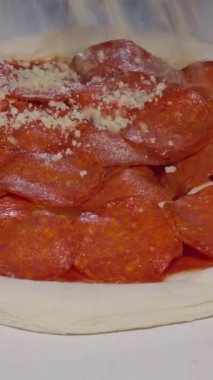 Dikey video. Pişmemiş Pepperoni Pizza üzerine ızgara peynir serpiştirme, Klasik İtalyan Rahatlatıcı Yemek Hazırlama Konsepti