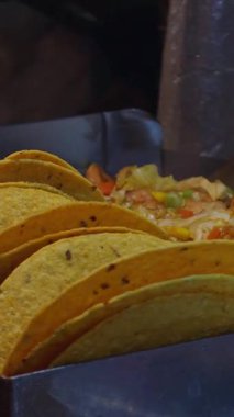 Dikey video. Izgara İstasyonu 'nda pişmiş tavuk ve sebzelerin yanında ayakta duran sert kabuklu tacolar, Meksika sokak yemekleri ve aşçılık geleneği kavramı.