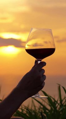 Dikey video. El kaldıran Kırmızı Şarap Kadehi Okyanus 'un Üzerinde Altın Gün Batımına Doğru, Yakın, Rahat Romantik Kavram