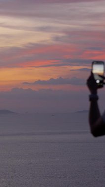 Dikey video. Akıllı Telefonu Tutan Kadın Okyanus, Arka Görünüm, Dijital Huzur Konsepti Üzerinde Canlı Gün Batımını Yakalıyor
