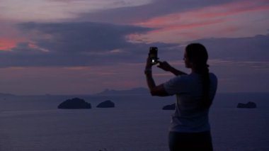 Gün batımında Smartphone, Rear View, Tranquil Reflection Concept ile Uzak Adaların Resmini Çeken Kadın