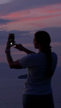 Dikey video. Gün batımında Smartphone, Rear View, Tranquil Reflection Concept ile Uzak Adaların Resmini Çeken Kadın