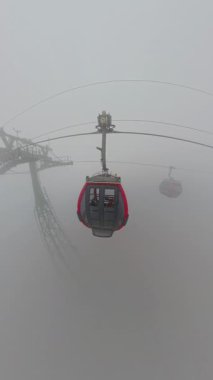 Dikey video. Ba Na Tepeleri 'ndeki yoğun sis destek kulesinin yakınından geçen kablo araçlar Geniş Açı Hava Görünümünde yakalandı
