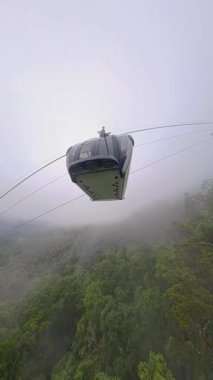 Dikey video. Ba Na Tepelerinde Düşük Puslu ve Bulut Katmanlı Yeşil Dağ yamaçlarında süzülen Kablo Araba Geniş Açı Hava Görünümü