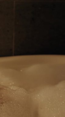 Dikey video. Derin Küvette Dinlenen Kadın Bacağında Köpük Tutarken Düşük Açı Vuruşu Rahatlatıcı Ruh Halini Vurguluyor