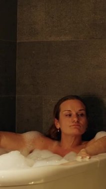 Dikey video. Kadın Küvette Köpükle Dinleniyor Bacağı Kaldırırken Musluğun yanında Bir Yan Bakış Açısı Görünümü Huzurlu bir Ruh Hali Oluşturuyor