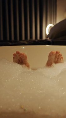 Dikey video. Düşük Açı Geniş Görünümlü Küvette Köpüklü Ayaklar Yumuşak Ilık Işıklı Sakin Bir Sahne Oluşturur