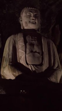 Dikey video. Geniş Açı, Ruhani Sembol Konsepti 'nde güçlü gölgeler yaratan, yumuşak yönlü ışıkta engebeli mağara duvarına karşı duran Büyük Taş Buda Heykeli.