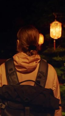 Dikey video. Gece Fener Yolu 'nun yanında duran gezgin. Kültürel Gece Yürüyüşü kavramını ifade eden Ilık Işıltı ve Orta Yol.