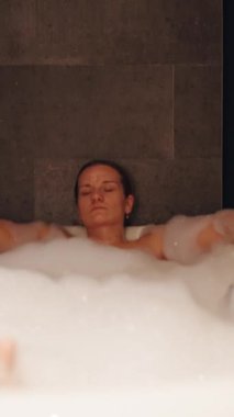 Dikey video. Orta Açı ve Yavaş Hareket Atmosferli Derin Köpük Banyo Tutma Kupası 'nda Dinlenen Kadın Spa Gevşeme Kavramını ifade ediyor