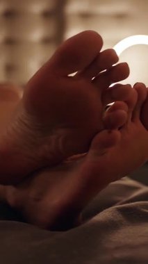 Dikey video. Otelin Yatağında Dinlenen Kadın Ayakları Sığ Derinlik ve Sıcaklık Işıltısı Rahatlık ve Akşam Rahatlığı Kavramını ifade ediyor