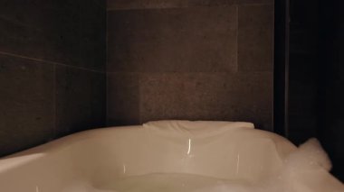 Otel Yatağında Dinlenen Kadın Işıklı Banyo ve Küvet 'in yanındaki telefonu kullanıyor. Düşük Açı ve Sıcak Ortam Işığı ile yakalanmış.