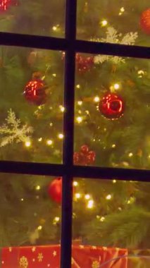 Dikey video. Pencerenin arkasındaki Noel Ağacını Kapat Parlak Kırmızı Süsler ve Parıldayan Işıklar Yumuşak Açı Görünümlü Sıcak Tatil Havası, Neşeli İç Modeli