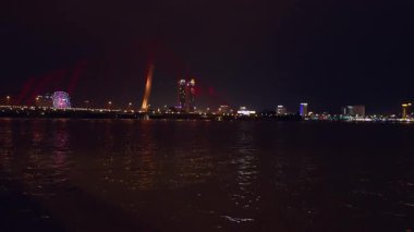 Parlak Kırmızı Işık Kablo Köprüsü, Dark River Water in Wide Angle View 'ı yansıtıyor. Şehir Işıkları ve dönme dolabı, canlı bir gece hareketi, akşam zamanı konsepti yaratıyor.
