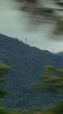 Dikey video. Dağların Önü 'nde Bulanık Yol Yaprakları Görünür Kablolu Arabalar Uzaktan Görünür, Görüntü Hareketi Konsepti