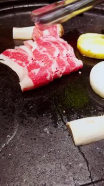 Dikey video. Çiğ sığır eti ince dilimleri mantar ve soğanın yanında kızarırken Tong 'lar Parlak lşık Altında Et Düzenliyor