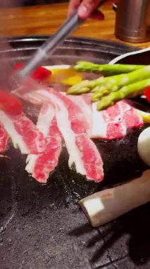 Dikey video. Buhar yükselirken ve içindekilerle birlikte elleri yana yatarken, Büyük Izgaraya Renkli Sebzeler Eklendi