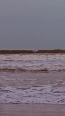 Dikey video. Geniş Açı Açı Çekimde Sakin Gök altında Kıyıya doğru Güçlü Dalgalar Çarpışıyor. Uzak Dağ Silüeti Kıyı Hava Durumu Konsepti İçin