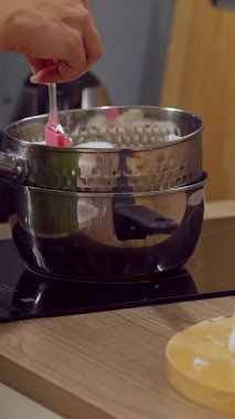 Dikey video. Erimeye Başlarken Geniş Açı 'da Spatula ile İkili Endüksiyon Sobası' na Balmumu Parçaları Ekleyen Kadın, El Yapımı Malı Konsepti