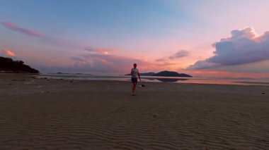 Geniş Açı İnsansız Hava Aracı, Sakin Deniz 'e yakın Geniş Kumsal' da Yörüngede Yürüyen Kadın Yörüngesinde, Güneş batarken Dramatik Bulutlar, Özgürlük ve Solo Seyahat Konsepti 'nin arkasında Parlıyor