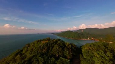 Pürüzsüz İHA İHA Uçuşu Yeşil Tepeler ve Tropikal Kıyı şeridi üzerinde Açık Gökyüzü Altında Yumuşak Akşam Işığı, Manzaralı Hava Yolculuğu Konseptiyle Açık Deniz 'e doğru yükseliyor.