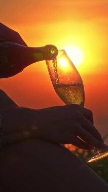 Dikey video. Kapalı Sinema Çekimi Çimlerde Oturan Köpüklü Şarabı Cama Döken Güneş Işığının Sıvı, Samimi Akşam Konsepti 'nden Geçişi sırasında