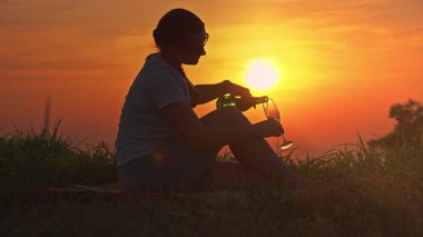 Çimlere Oturan Kadının Yakın Çekimi Yeşil Şişe 'den Parlak Güneş Arkaplanda, Kutlama Konsepti ile Cam' e Köpüklü Şarap Döküyor