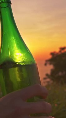 Dikey video. Yakın çekim Elde Tutulan Şampanya Şişe Yumuşak odaklı Altın Gün batımına karşı Deniz Ufku ve Sıcak Akşam Işığı, Kutlama Konsepti